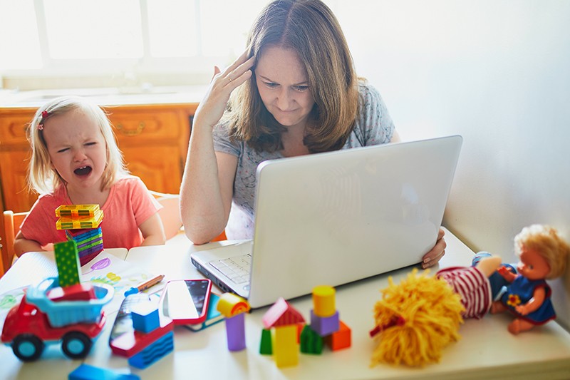 Exhausted and stressed mother working from home with toddler